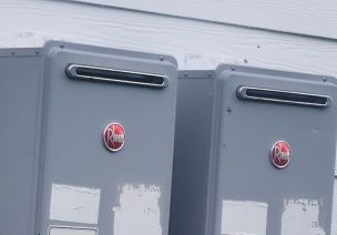 2 tankless water heaters mounted on the side of the house next to each other. Picture to describe 2 units to be serviced